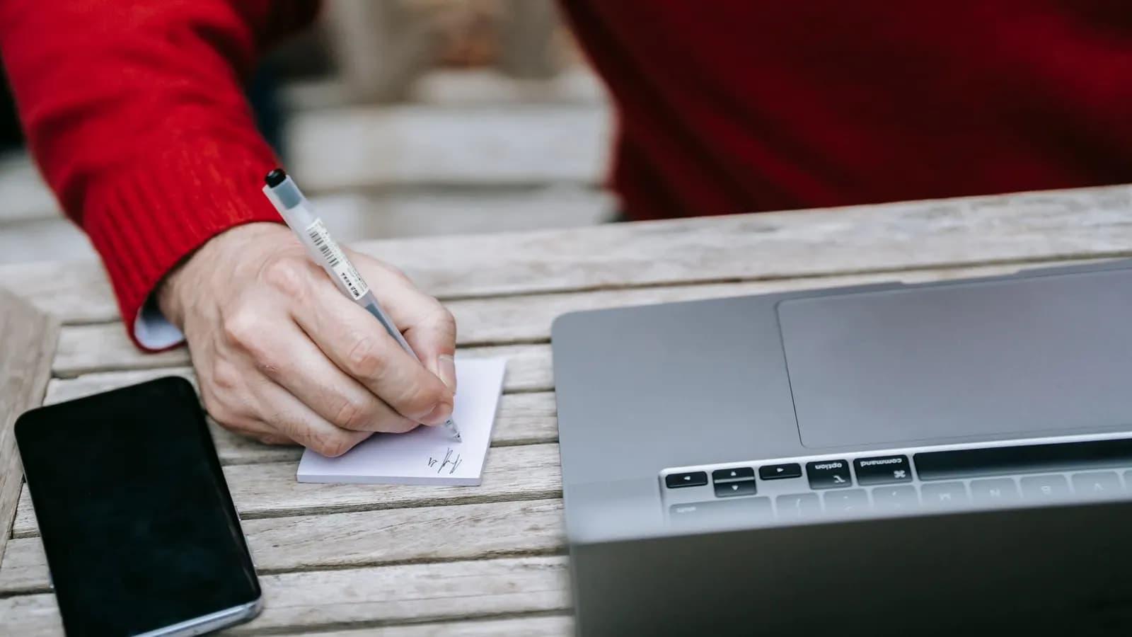 Seseorang menulis catatan di buku sambil bekerja di depan laptop