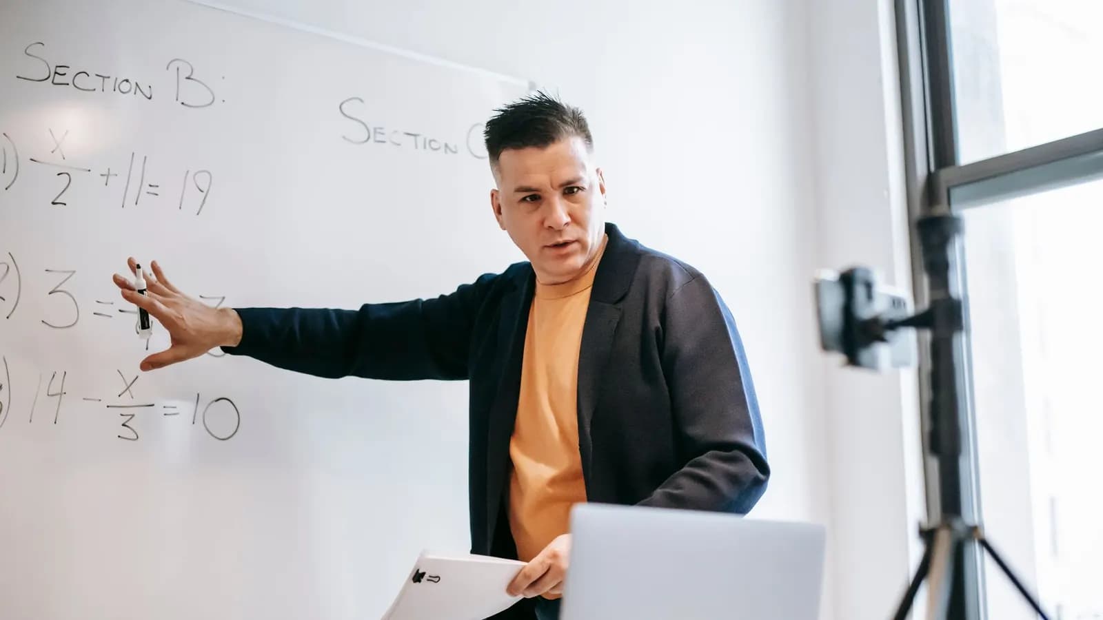 Seorang pengajar merekam kelas daring di depan laptop dan kamera